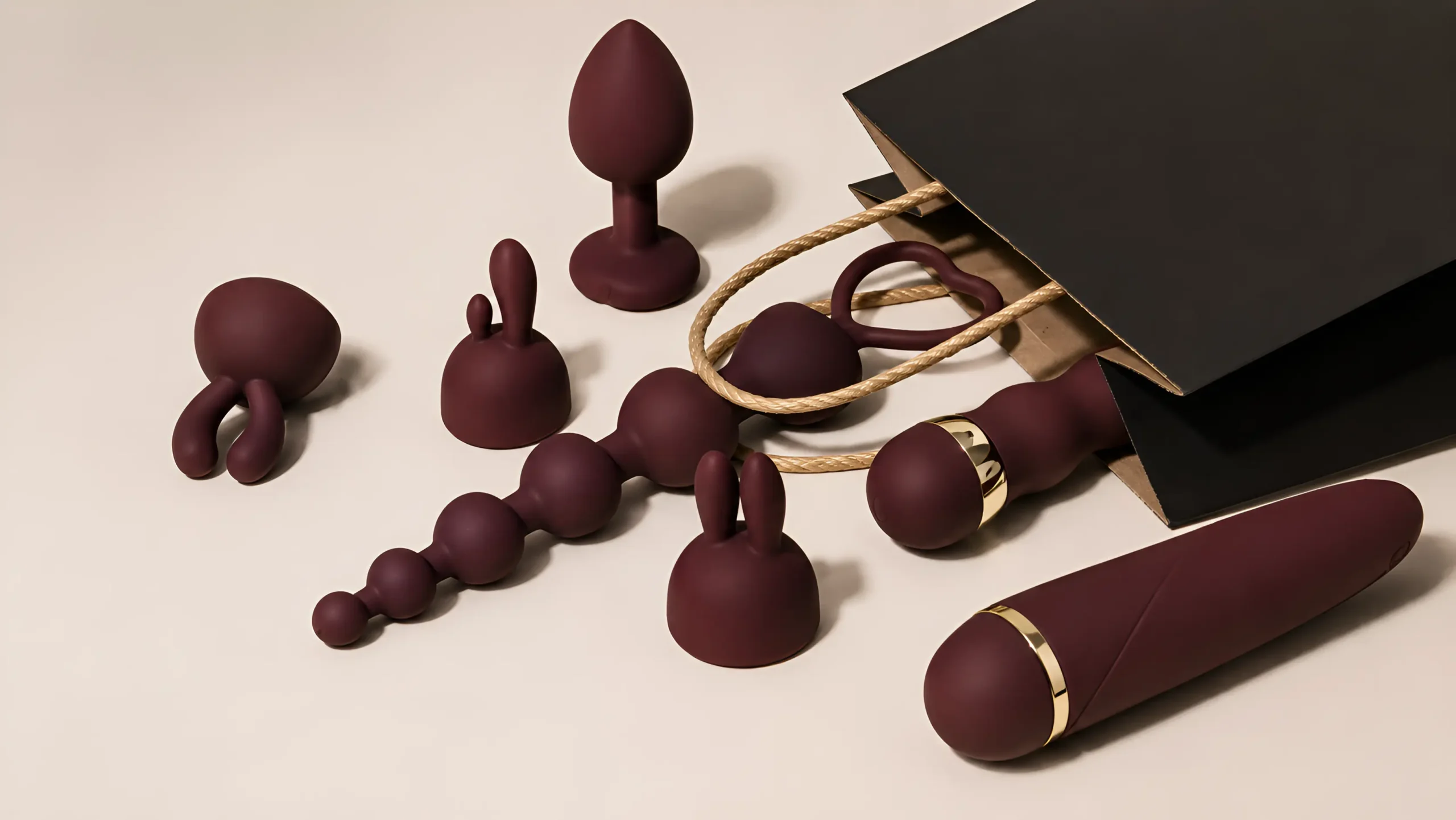 Beginner-friendly sex toys arranged beside black gift bags on a warm ivory surface